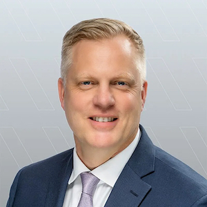 A slightly smiling blond man in a blue suit