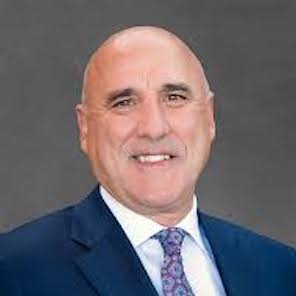 A close up of an older man in a nice suit looking into the camera and smiling.